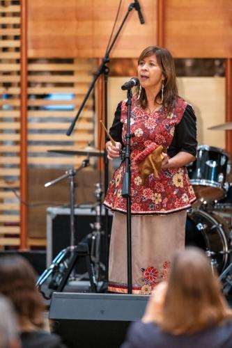 A woman dressed in a floral vest and skirt performs on stage