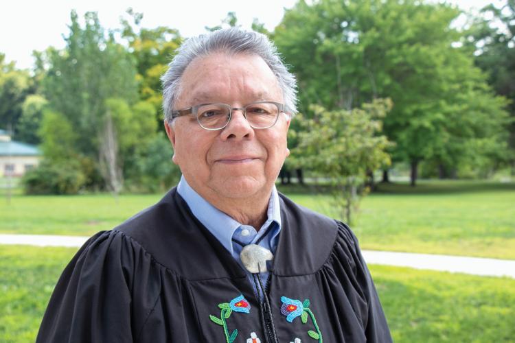 A portrait of Michael Petoskey, a man with grey hair and glasses, wearing a black robe with floral designs