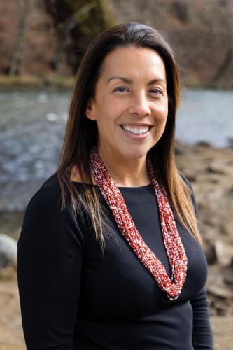 A portrait of a woman with long brown hair, wearing black clothing and a red necklace