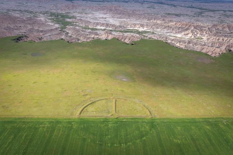 An aerial view of an expanse of land. In the center, a target made of mounded earth is visible.