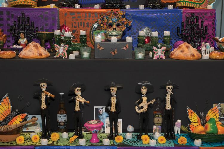 An altar decorated with monarch butterflies, food, marigolds, and skeleton figures