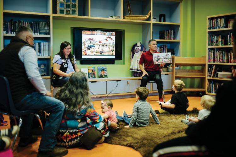 A man holds a picture book up to a group of young children and accompanying adults