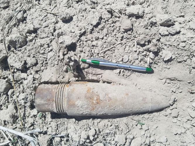 A World War II rocket warhead about the size of a football lies on rocky ground with a pen next to it for scale