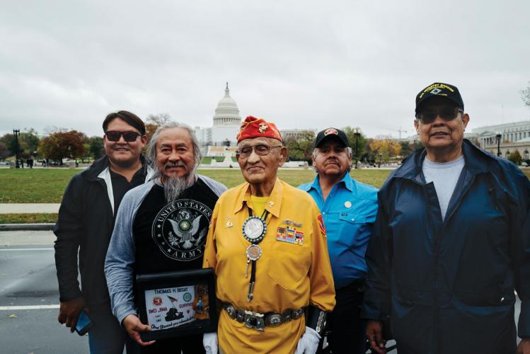 A veteran dressed in yellow and decorated with medals is flanked by four other men