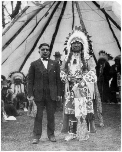 Archival photo of a son of a Shoshone chief in a feathered headdress and an interpreter