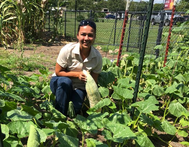 A Cherokee woman crouches in a garden, holding a squash