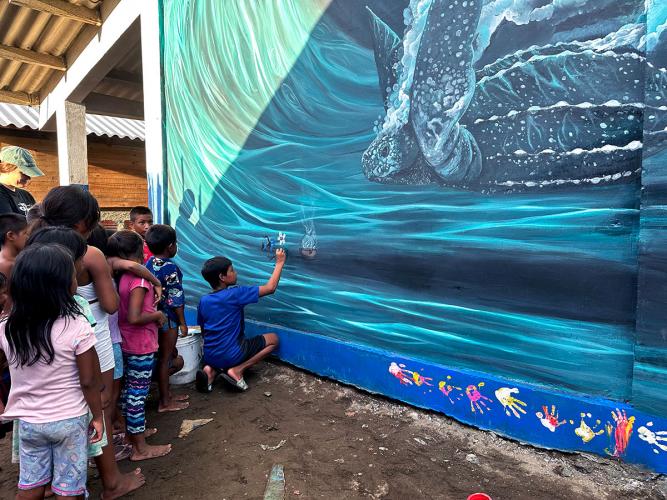 Young people observe and contribute to a large mural of a sea turtle