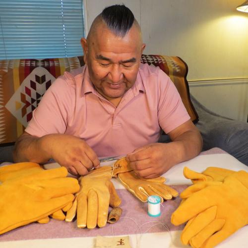 A man sits at a table, crafting gloves from tanned hide