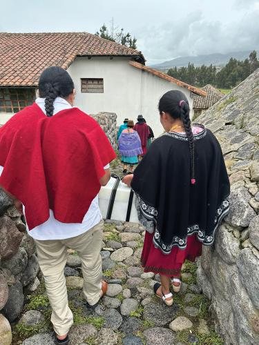 Two people escort a box of ancestral remains down a stone path toward a building