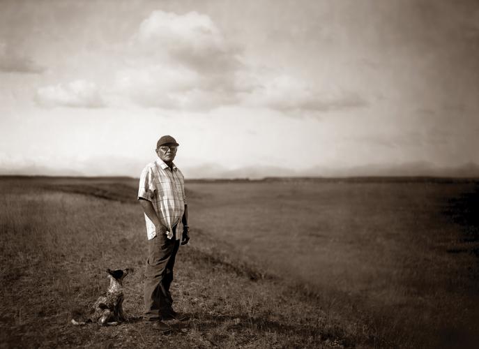 A sepia photograph of a man standing in an open landscape, with a dog at his feet