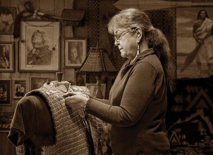 A sepia photograph of a woman standing and sewing a cedar bark vest