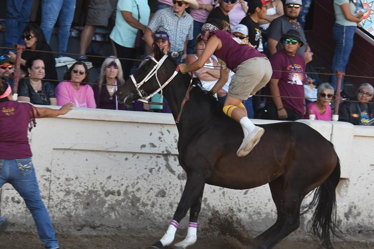 A rider dismounts a racehorse restrained by a holder