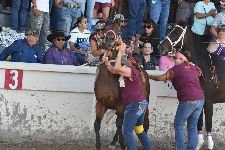 A rider mounts a racehorse, having just dismounted another horse restrained by a holder