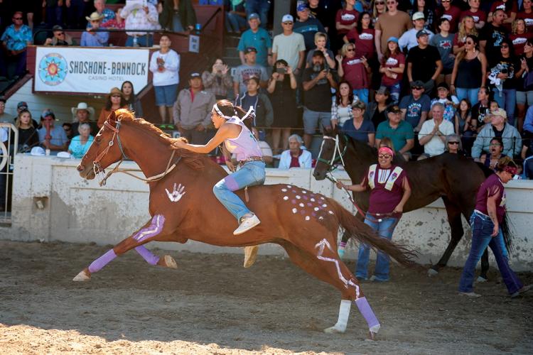 A rider races a horse decorated with painted symbols in front of a crowd of spectators