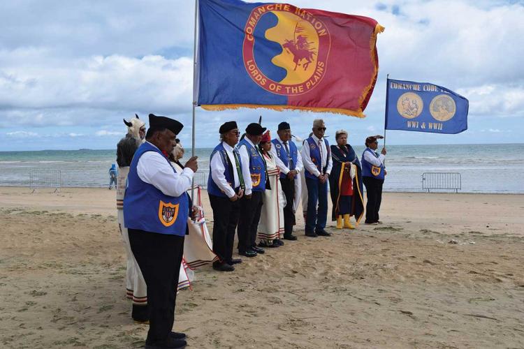 People stand in a line on a beach, holding several large flags
