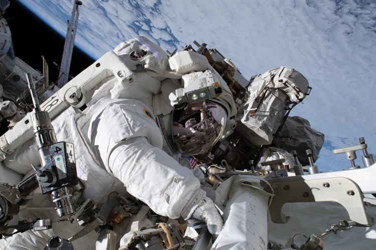 Astronaut Nicole Mann in a space suit working on the exterior of the International Space Station with Earth visible in the background