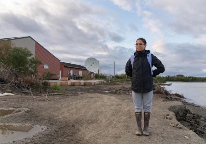 Student Madison Andrew standing near a school house on the shore of the Kuskowim River.