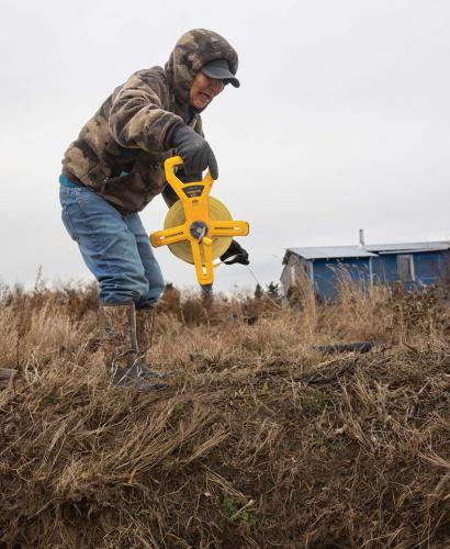Person using handheld tape measure along river bank.