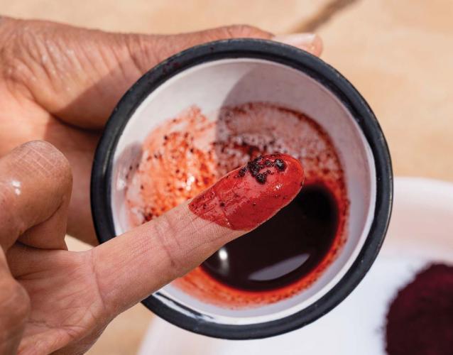 Close up of DY Begay's hands holding a bowl of deep red fabric dye.
