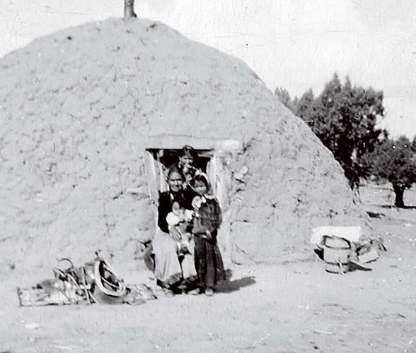 Black and white archival photo of a grandmother and child in the doorway of a domed hogan.