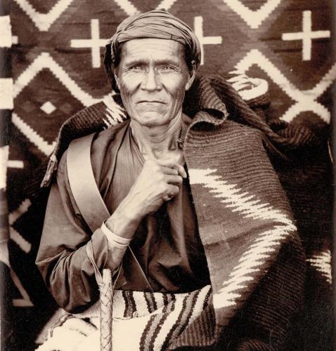 A black and white archival photo of a man wrapped in a patterned blanket.