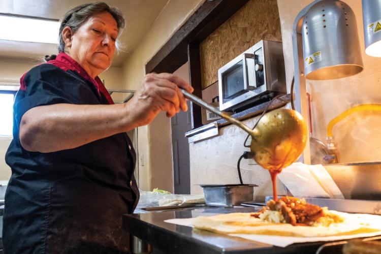 Person serving a breakfast burrito with chili.
