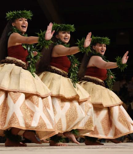 Hula dancers perform on stage in long woven bark shirts