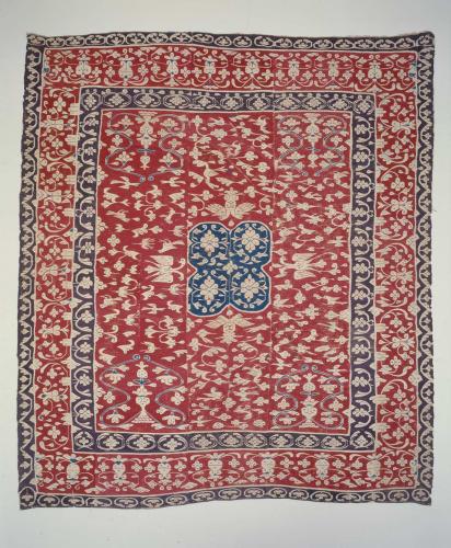 Woven red poncho with blue trim and depictions of flowers and birds