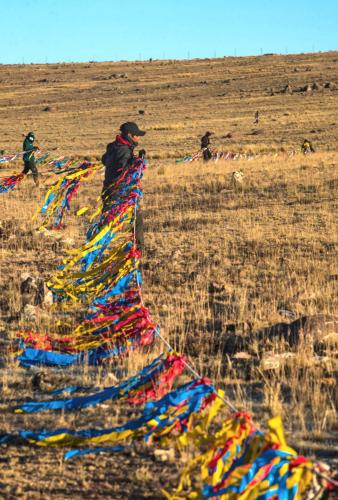People carrying a rope covered in colorful ribbons walk across alpine tundra