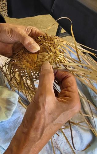 Hands weaving leaves into crown of hat