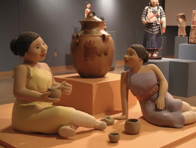 Two clay sculptures on display in an art gallery depicting two sisters making pottery