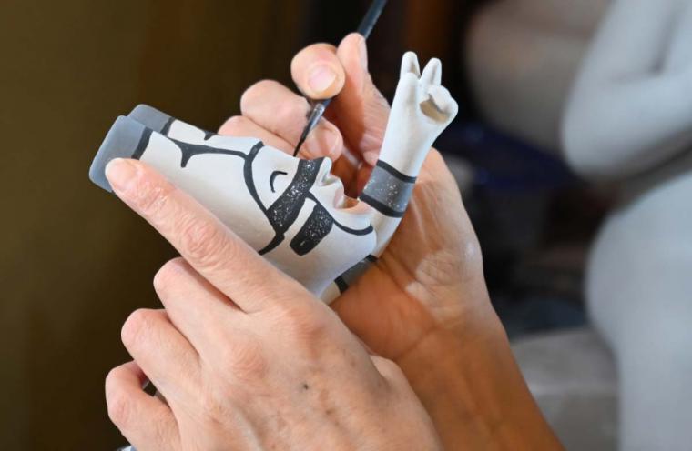 Kathleen Wall paints a small clay figure with a brush