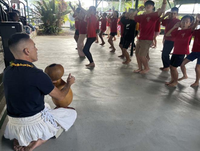 Youth practicing hula moves while instructor beats on drum