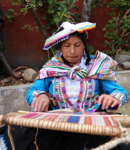 Weaver in colorful dress weaves a shall on a loom 