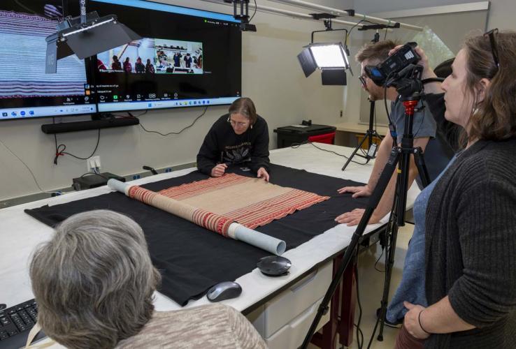 Museum workers display a colorful textile on a tabletop.