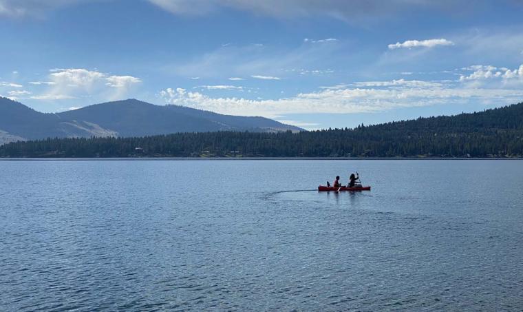 Two people paddle a canoe in the open waters of a large lake with mountains in the background.