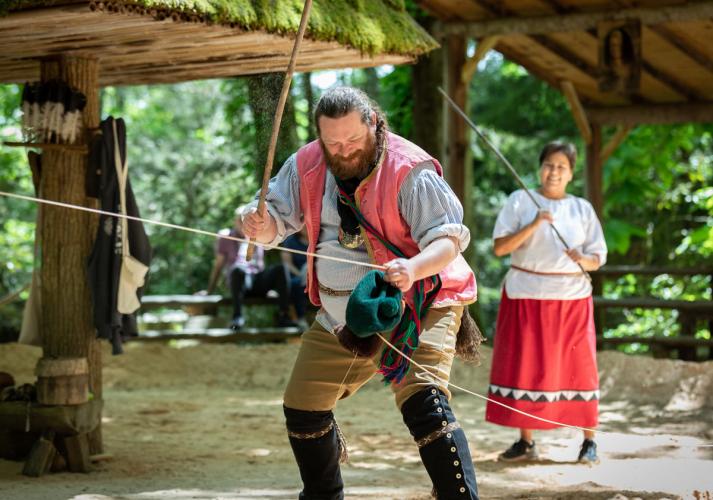 A person in a red vest holds a rope and a stick.