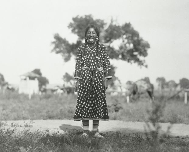 A black and white image of a 10-year-old girl in a dress sticking her tongue out.