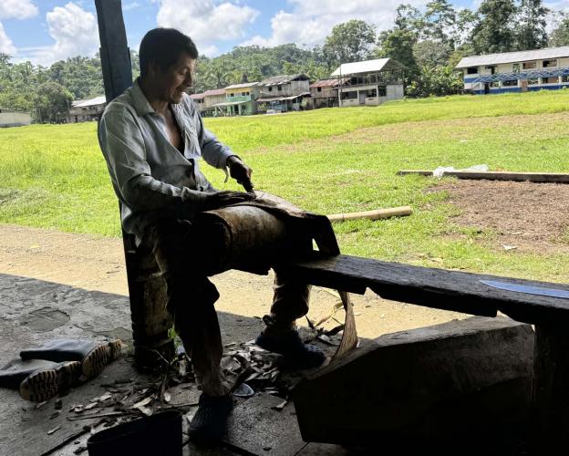 Person sits on bench scraping a roll of tree bark.
