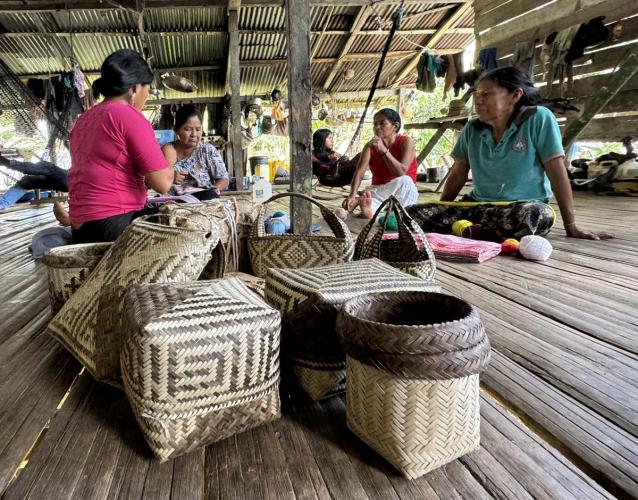 Group of weavers sitting on floor with woven baskets.