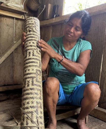Weaver dressed in blue displays a finished mat.
