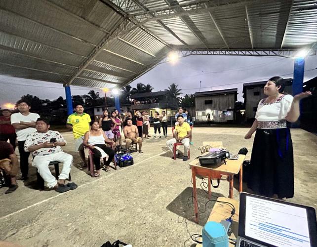 Community members gather in an open air field house to view presentation.