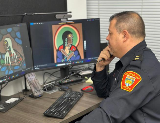 Police officer compares work on two monitors.
