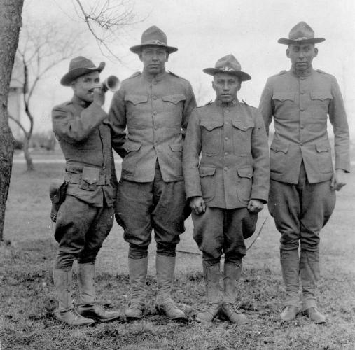 Four soldiers, one playing a bugle, stand in line