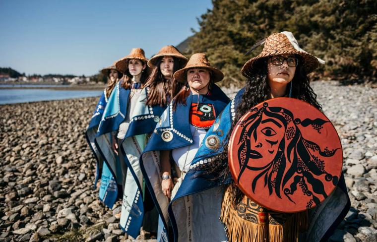Members of the herring protectors group wearing cloaks with the first woman carrying a shield on a beach.