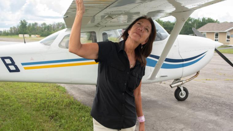 Jo-Anne Tabobandung stands beneath and holds the wing of her aircraft.
