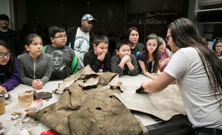 A workshop instructor talks about tanning moose hides to a crowd of children