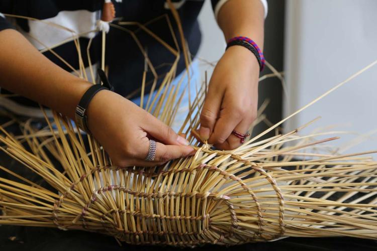 Hands stitch together dried seagrass.