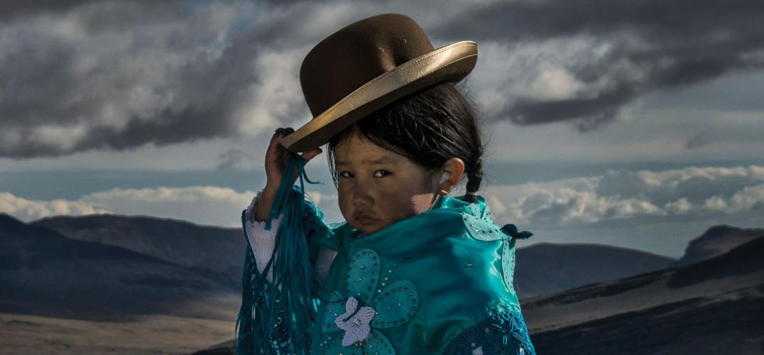 Young Bolivian girl in traditional cholita attire tips her bowler hat