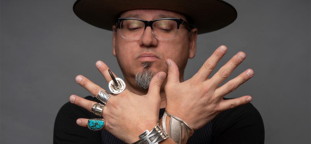 Artist Erik Lee holding up his hands, showing silver rings and bracelets he created